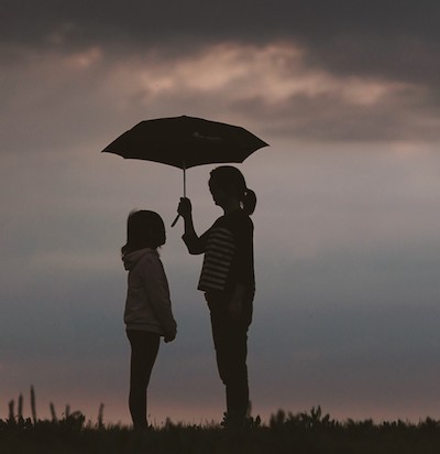Mother and daughter stand under an umbrella with a scenic sky behind them