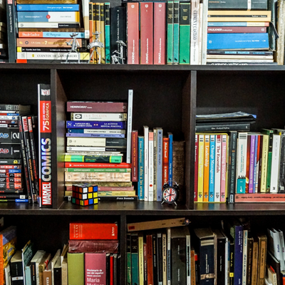 Black bookshelf filled with books and a few knick-knacks. The books are stacked in rows beside each other and on top of each other