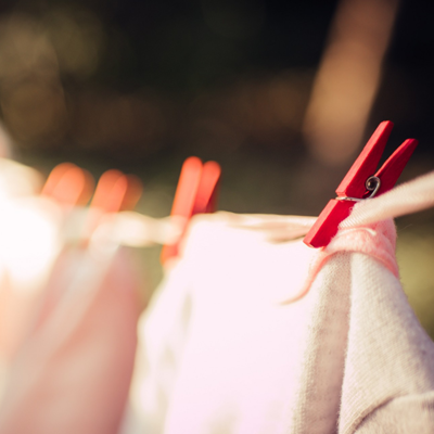 A white piece of clothing on an outdoor clothesline. The clothespin is red and the background of the picture blurs.