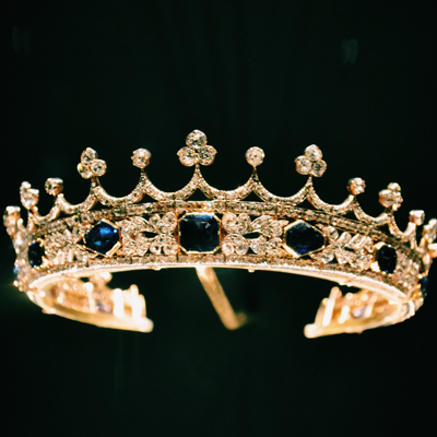 A golden crown (embedded with diamonds and dark blue gems) sits on a black background.