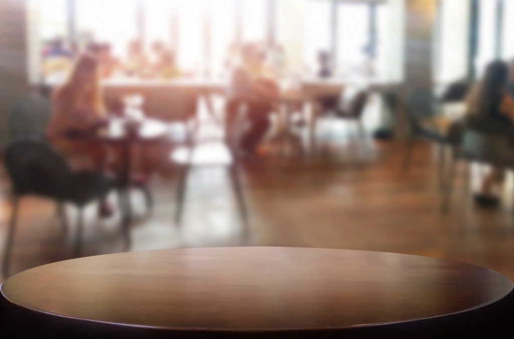 A picture of people eating in a communal dining area. The picture has a forced perspective, with the lens focusing on the table at the front of the camera, while those eating are blurred.