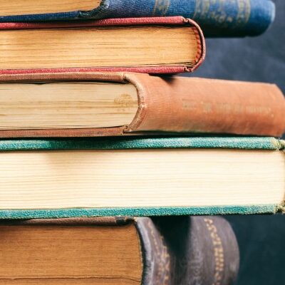 A stack of books sits on a table against a dark blue backdrop