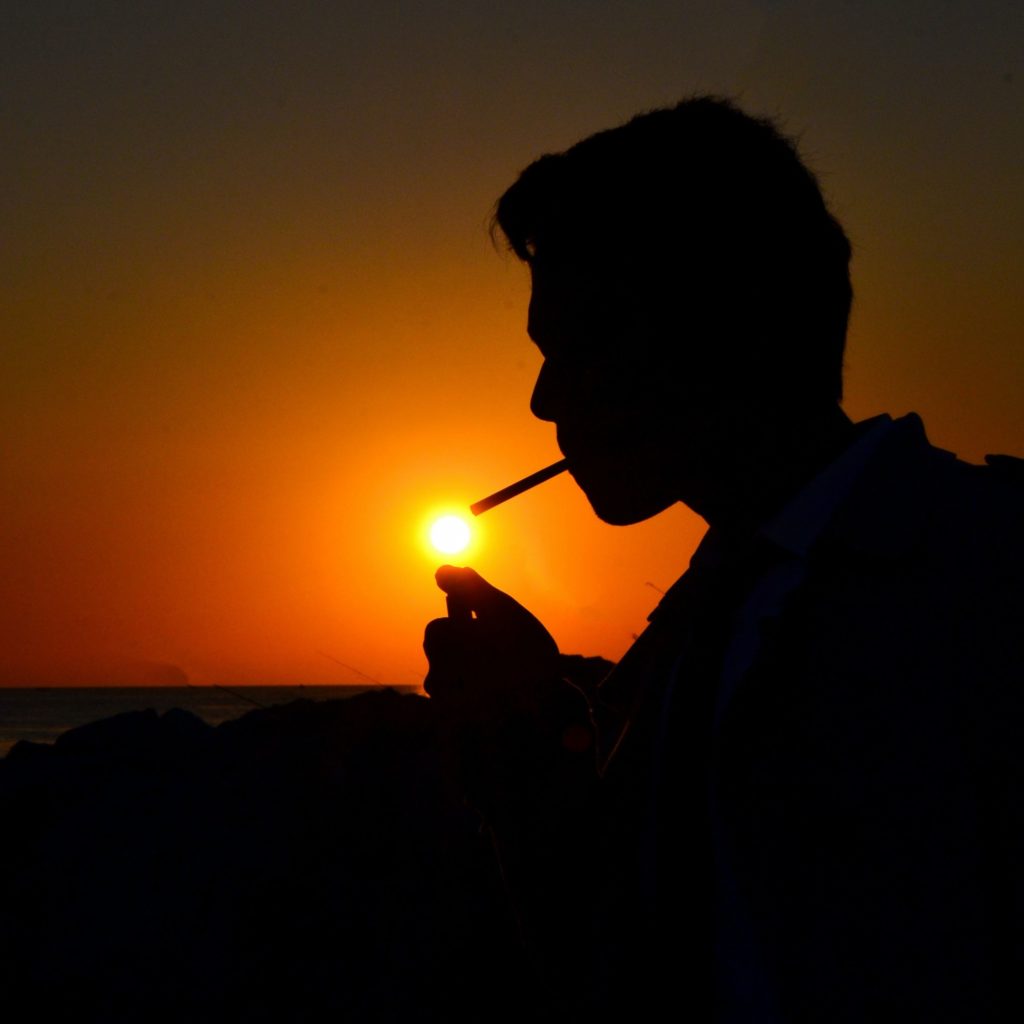 Silhouette of person smoking at sunset, with the sun looking like the flame of the lighter