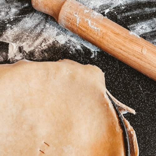 A pie and a rolling pin sitting amid flour.